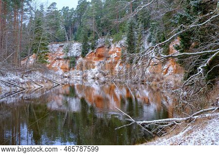 View Of Red Sandstone Cliffs. Salaca River. Skanaiskalns Nature Park. November Is The First Snow In 
