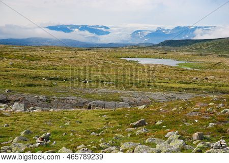 Raw Norwegian Landscape - Panorama, View Of Pastures, Lake And Mountains In Clouds Covered With Snow