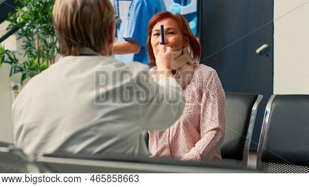 Physician Doing Consultation With Asian Woman In Hospital Lobby, Wearing Cervical Collar. Patient Wi