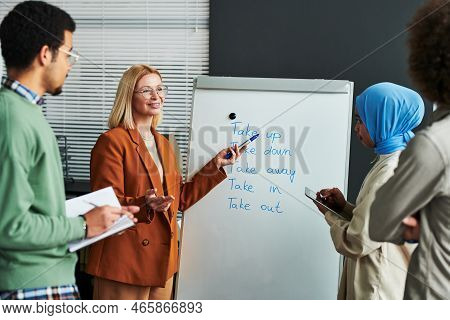 Confident Mature Teacher Of English Language Pointing At Whiteboard
