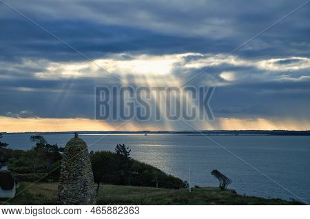On The Coast Of Hundested. Sun Rays Break Through The Dramatic Sky Through The Clouds. Meadow With S