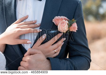 Bride's Hands On The Groom's Boutonniere. Wedding Decor For The Wedding Ceremony Of Flowers For Even