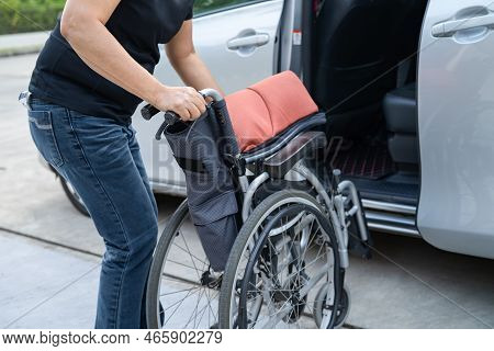 Asian Woman Folding And Lift Up Wheelchair Into Her Car. Accessibility Concept.