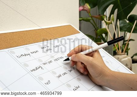 Female Hand Writing With Marker On Monthly Planner Filled With Appointments And Plans For Next Month