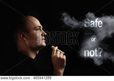 E-cigarette Safe Or Not. A Young Man Smokes An Electronic Cigarette Against A Black Background And B