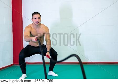A Handsome Muscular Young Man Using Battle Ropes For Exercise In A Gym. Look At Camera. Motivational
