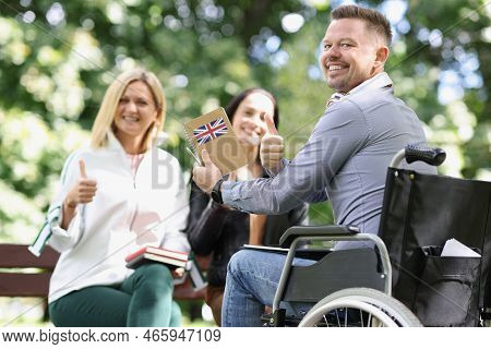 Portrait Of Smiling Disabled Man In Wheelchair Studying English With Friends And Showing Thumbup Sig