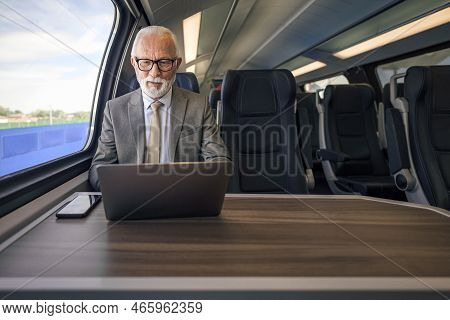 Senior Businessman Working On Laptop While Sitting On Passenger Train. Male Entrepreneur Is Wearing 