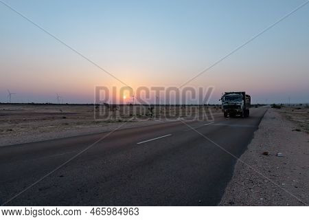 Dawn Light In Desert Sky With Empty Road Passing Through The Desert. Wind Mills In The Horizon, Sun 
