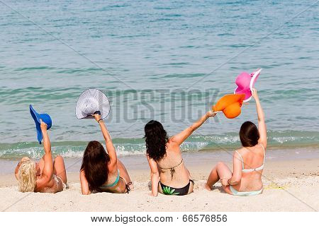 Back View Of Four Young Playful Women In Summer Hats Resting On The Beach And Enjoy The Tropical Sea