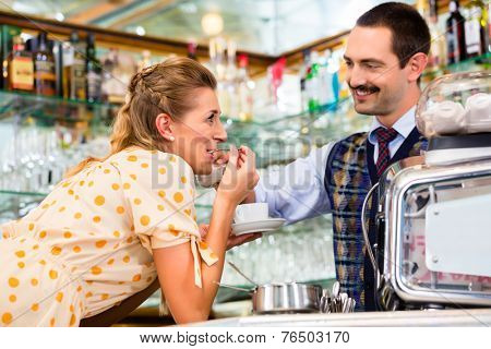 Girl in cafe or coffee bar flirting with barista who is busy preparing Cappuccino with professional machine