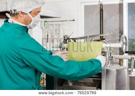 Side view of chef preparing green pasta sheet in machine at commercial kitchen