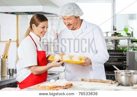 Smiling male and female chefs holding pasta tray in commercial kitchen