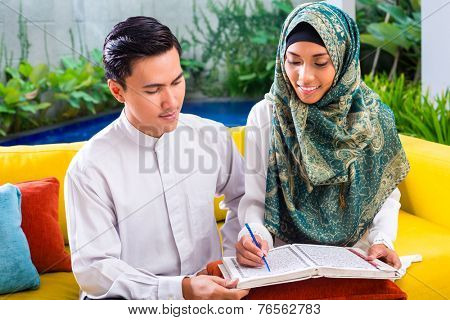 Asian Muslim man teaching woman reading Koran or Quran in living room