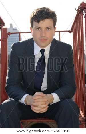 Muž v obleku sedí na požárním schodišti