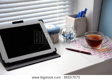 PC tablet, notebook and cup of tea on windowsill. Working place concept