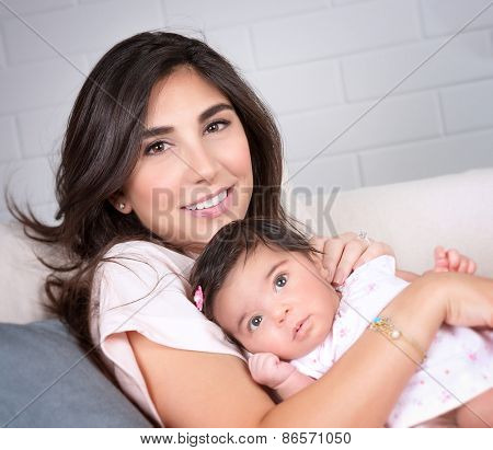 Closeup portrait of beautiful brunette mother with cute newborn daughter relaxing on sofa at home, happy young arabic family