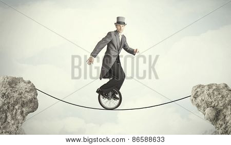 Brave business man riding an mono cycle between cliffs concept