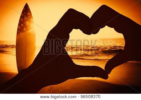 Couple making heart shape with hands against surf board standing on the sand