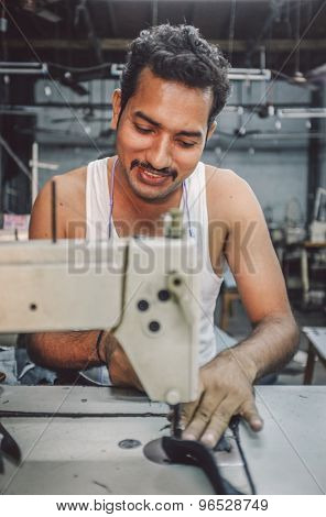 MUMBAI, INDIA - 12 JANUARY 2015: Indian worker sews in clothing factory in Dharavi slum. Post-processed with grain, texture and colour effect.