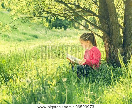Cute little girl read the book under tree