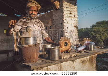 GODWAR REGION, INDIA - 14 FEBRUARY 2015: Man prepares milk tea with traditional wind turbine for making fire. Post-processed with grain, texture and colour effect.
