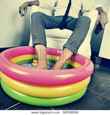 a young man in suit soaking his feet in an inflatable water pool indoors, with a dramatic effect, depicting the concept of staying at home on vacation