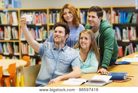 people, technology, education and school concept - happy students or friends with smartphone taking selfie in library