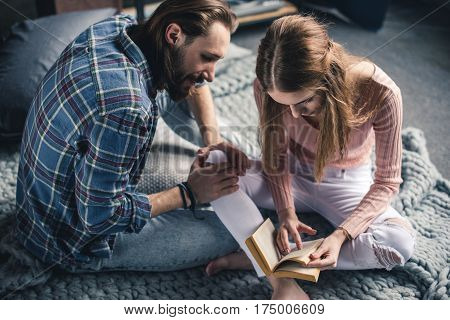 Young barefoot couple sitting on knitted blanket and reading book