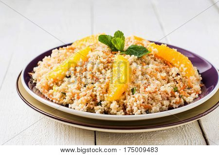 Useful fresh salad of crumbly couscous with carrots orange and mint in a bowl closeup on white wooden table. Dietary vegetarian food traditional Mediterranean cuisine recipes. Selective focus