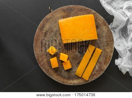 Block slices and cubes cheddar cheese on a wooden cutting board