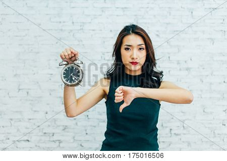 Asian Business Woman Showing Thumbs Down And Holding Alarm Clock - Indicating That Not Pleased With
