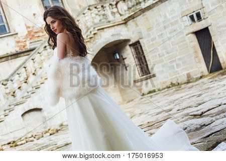 Young sexy girl with long hair and pretty face in white wedding bride dress posing near castle or palace building