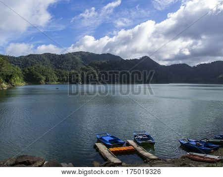 Lake and mountains landscape with colorful boats. Empty bay on volcanic lake. Sunny day on natural travel journey. Volcanic lake surrounded by forest mountains. Sunny weather and wild nature scene