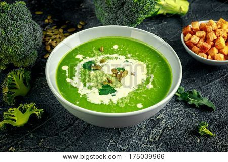 Dietary Broccoli smooth cream soup with sprinkle of sunflower seeds, parsley leaves and croutons on stone table
