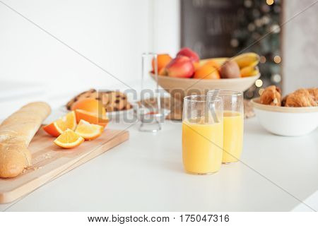 Plate of tasty cookies with chocolate crumbs, croissant, baget, bananas, apples, persimmon, orange and orange juice on white table.
