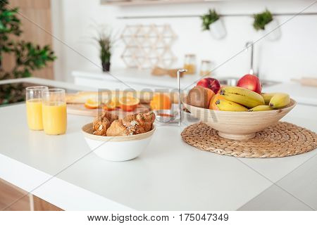 Plate of tasty cookies with chocolate crumbs, croissant, baget, bananas, apples, persimmon, orange and orange juice on white table.
