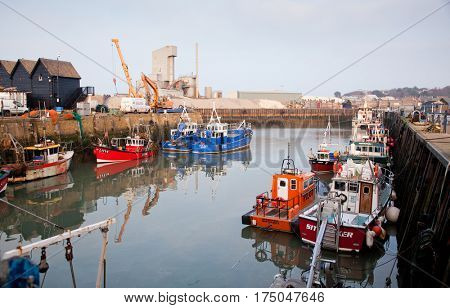 WHITSTABLE, UK -February 24, 2017: Fishing Boats in Whitstable Harbour in portrait view with warehouse in background