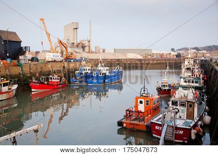 WHITSTABLE, UK -February 24, 2017: Fishing Boats in Whitstable Harbour in portrait view with warehouse in background