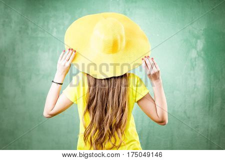 Colorful portrait of a beautiful woman in yellow t-shirt and hat on the green background. Back view
