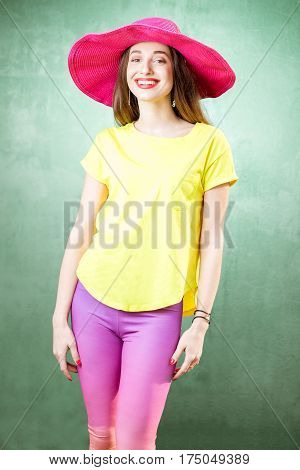 Colorful portrait of a beautiful woman in yellow t-shirt and pink hat on the green background