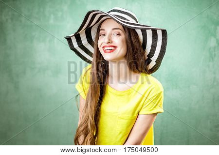 Colorful portrait of a beautiful woman in yellow t-shirt and striped hat on the green background
