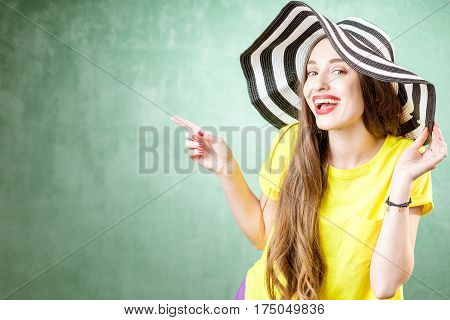 Colorful portrait of a beautiful woman in yellow t-shirt and striped hat on the green background