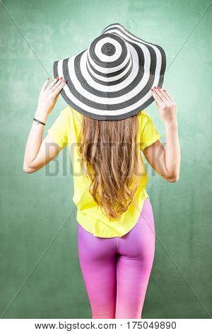 Colorful portrait of a beautiful woman in yellow t-shirt and striped hat on the green background