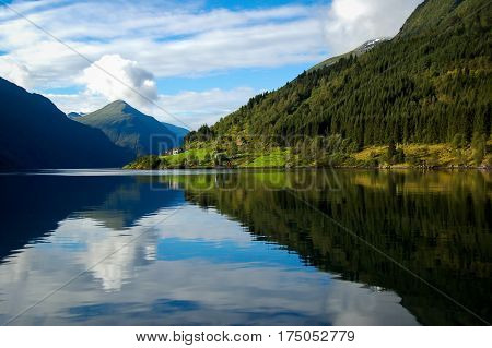 gudvangen fjord in norway refleting on the water on a blue sky with clouds background