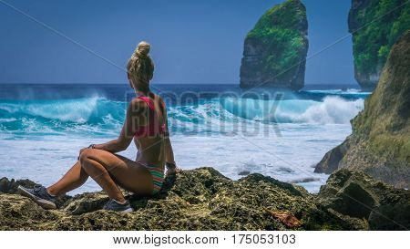 Girl sitting on the Rock and watching Huge Waves hitting Tembeling Coastline at Nusa Penida Island, Bali Indonesia.