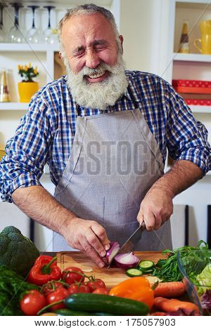 Close-up of mature man chopping an onion. Stinging eyes and tears when cutting onions to prepare dinner. Shedding tears and wiping with the back of her hand. Man crying while chopping an onion 