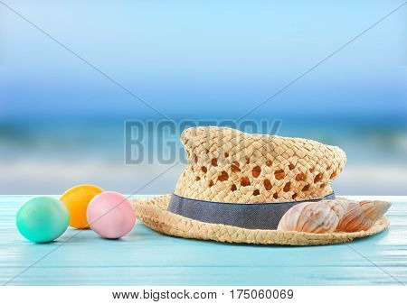 Easter eggs with hat and seashells on wooden table at shore