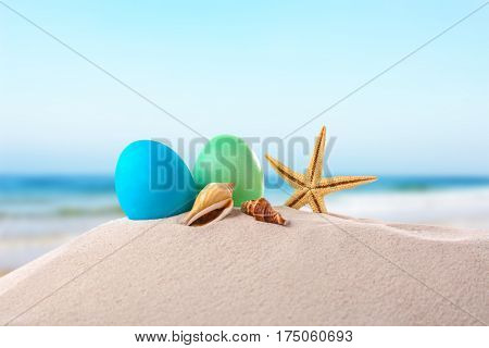 Easter eggs with seashells on sand at shore