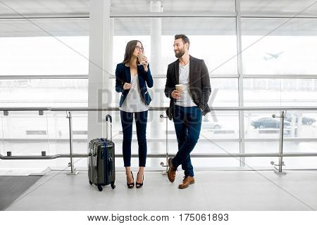Business couple standing together with baggage and coffee cups near the window at the departure area at the airport